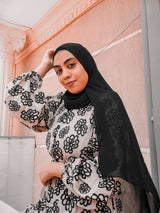 woman against pink tile with black hijab black and white floral abaya