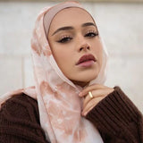 woman in pink and white tye die hijab with beige undercap and brown sweater marble block background